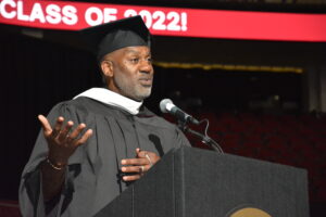 Keith Dawkins '94 in a cap and gown at the podium addressing the Class of 2022 at the 69ɫƵ Commencement