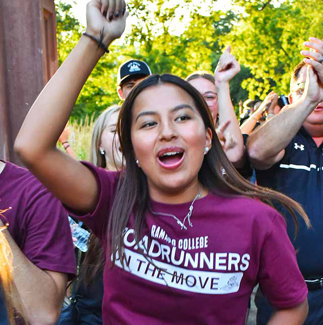 Student wearing a maroon 69ɫƵ t-shirt, cheering by the arch